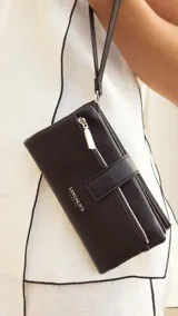 Billetera Lincoln's de mujer en color negro, confeccionada en símil cuero con textura granulada. Presenta un diseño rectangular con cierre de broche, bolsillo frontal con cierre metálico, correa de mano extraíble y logo de la marca grabado en el frente.