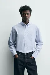 Camisa de corte regular fit confeccionada en tejido de algodón con diseño de rayas verticales finas. Presenta cuello abotonado, manga larga con puños abotonados, bolsillo plastrón en el pecho y cierre frontal con botones.