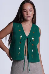 Chaleco tejido negro con bordado de flores blancas y naranjas, con lazos de ajuste en el frente.