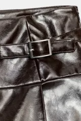 Falda corta de tiro medio con acabado efecto piel brillante. Presenta detalle de trabillas con hebillas metálicas en la parte frontal y cierre lateral con cremallera oculta.