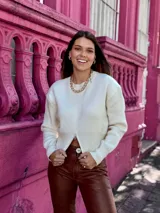 Suéter de punto color crema, con cuello redondo, manga larga y cierre frontal parcial que deja ver parte del abdomen.