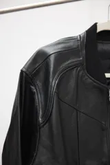 Campera tipo bomber de cuero ovino color marrón oscuro, con cuello de tejido acanalado y cierre frontal con cremallera.