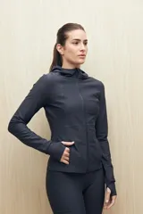 Campera deportiva negra de calce entallado, con cierre frontal completo, capucha integrada y mangas largas con puños envolventes. Presenta costuras estratégicas que estilizan la silueta y bolsillos laterales funcionales.