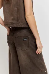 Pantalón de denim estilo wide leg color marrón gastado, con apliques de tachas metálicas o strass distribuidos por toda la prenda y tiro medio.