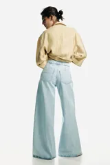 Jean de denim de algodón rígido, de color celeste claro, con tiro alto y pierna amplia de corte extraholgado. Presenta diseño clásico de cinco bolsillos, cierre frontal con cremallera y botón metálico.