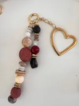 Colgante decorativo para bolso o llavero, compuesto por una cadena metálica con un conjunto de cuentas de diferentes formas, colores y texturas, incluyendo piedras naturales y cuentas de madera.