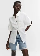 Camisa blanca de lino con cuello clásico, manga corta, corte oversize, cierre frontal con botones y bolsillo de parche en el pecho.