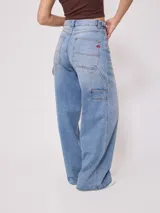 Jean de corte baggy y tiro medio, confeccionado en denim de algodón en tono azul claro con efecto lavado. Presenta diseño de cinco bolsillos, cierre frontal con botón y cremallera, y pernera ancha.