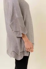 Buzo de tejido liviano con brillo sutil tipo lurex, color beige o dorado claro. Presenta un calce suelto (oversize) con mangas amplias y cuello redondo. El ruedo tiene un detalle de terminación festoneado con pequeños calados.