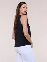 Blusa sin mangas de seda fría marca Rio & Rian, color blanco con ribetes negros en cuello y sisas. Presenta un escote redondo con abertura tipo gota en el frente y un aplique metálico decorativo.