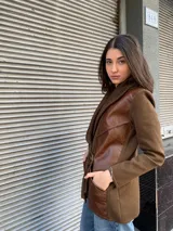 Chaqueta de punto color marrón con cuello de punto acanalado y solapas de cuero. Presenta un cinturón de tela con hebilla dorada y bolsillos de cuero con detalles de cordones.