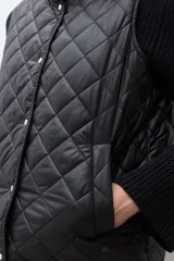 Chaleco acolchado con diseño bicolor, presentando la parte superior en verde oliva y la parte inferior en beige. Cuenta con cierre frontal de botones a presión, cuello alto y dos bolsillos delanteros amplios con borde en contraste.