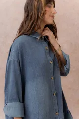 Vestido camisero corto de denim liviano azul con efecto desgastado, de corte oversize, con cuello camisero, botonadura frontal, bolsillo plaqué en el pecho, mangas largas y volado fruncido en el ruedo.
