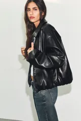 Chaqueta bomber de efecto piel con cuello solapa, cierre frontal de cremallera metálica, bolsillos laterales de vivo y bajo y puños con elástico.