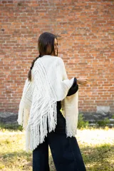 Ruana tejida en crochet de lana merino color crudo, con diseño abierto y flecos decorativos en el ruedo.