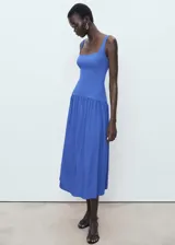 Vestido midi de color azul, con diseño evasé, cuello cuadrado y tirantes anchos. Presenta un corte en la cintura con falda fruncida y cierre de cremallera en la parte posterior.