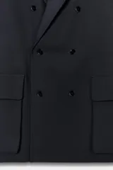 Blazer oversize de corte recto con cuello solapa y cierre frontal cruzado con botones. Presenta mangas largas con hombreras, trabillas en los hombros y grandes bolsillos de plastrón con solapa en el delantero. Incluye abertura en la espalda y forro interior.