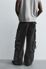 Pantalón cargo de denim lavado negro, corte relajado y tiro medio. Presenta múltiples bolsillos cargo con solapa y detalle de cierre en las perneras, además de bolsillos de vivo traseros. El bajo es ajustable con trabilla.