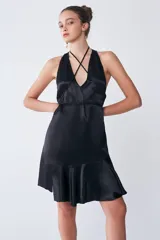 Vestido midi negro de tejido sastrero fino y liso con leve brillo. Tiene escote en V, tiras para ajustar en la cintura, volado asimétrico en el ruedo y espalda descubierta.