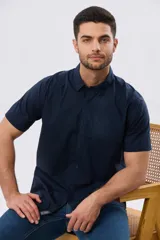 Camisa lisa de algodón azul marino, de manga corta, con cuello camisero, cierre frontal de botones y un bolsillo aplicado en el pecho.
