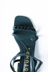Sandalias de taco cuadrado medio, confeccionadas en gamuza color azul. Presentan tiras finas que cruzan el empeine, una pulsera ajustable al tobillo y detalle de cuentas decorativas en la tira frontal.