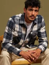 Camisa a cuadros azul marino y beige, de manga larga, con cuello clásico y dos bolsillos con solapa abotonada en el pecho.