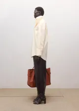 Blusa oversize de algodón en color marfil, con cuello camisero alto, manga larga con puños abotonados y cierre frontal de botonadura oculta.