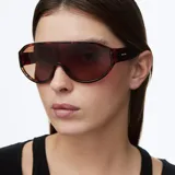 Lentes de sol con diseño envolvente tipo máscara y lente panorámica color marrón. Montura con estampado carey, ofreciendo un estilo técnico y deportivo.