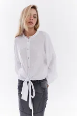 Camisa blanca de lino italiano, de corte holgado, mangas largas abullonadas, cuello mao y cierre frontal con botones, con diseño para anudar en la cintura.