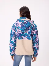 Campera tipo canguro con diseño combinado, parte superior estampada con flores en tonos azules y rosados, y parte inferior de tejido sherpa en color beige. Cuenta con cuello alto, cierre frontal parcial y bolsillo tipo canguro delantero con logo de la marca.