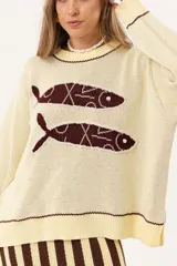 Sweater color manteca de tejido de punto con cuello redondo y ribete marrón. Presenta dos peces marrones tejidos en el frente con detalles bordados a mano.