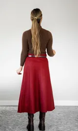 Pollera midi de corte irregular con diseño de estampado cuadrillé en tonos rojo y negro. Presenta un acabado con flecos en el borde y una abertura lateral que deja ver la pierna.