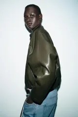 Chaqueta estilo bomber de efecto piel en color verde oliva, con cuello solapa, cierre frontal con cremallera, mangas largas y bajo elástico.