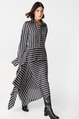 Camisa de corte holgado con estampado de cuadros en tonos marrones y beige. Presenta cuello clásico, cierre frontal con botones y mangas largas con aberturas laterales que permiten anudar la prenda en la cintura.