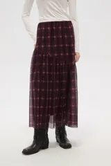 Falda larga de corte evasé con estampado de cuadros escoceses en tonos bordó y negro. Presenta un diseño de doble capa con una base opaca y una sobrecapa de tul semitransparente, con un corte asimétrico en la parte inferior.