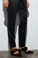 Zapato de tacón color negro, con punta fina y confeccionado en gamuza. Presenta un nudo decorativo en el empeine y pulsera con hebilla dorada.