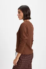 Remera de manga larga con textura acanalada y silueta ajustada. Presenta cuello redondo y un pequeño bordado decorativo en el centro del pecho.