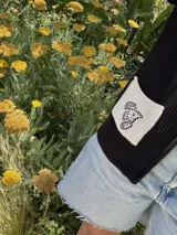 Campera tejida con textura vanizada a rayas horizontales en blanco y negro, con cierre frontal y flecos negros en forma de V en el pecho.