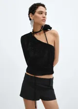 Blusa asimétrica de terciopelo negro con textura de flores en relieve, diseño de un solo hombro con manga larga y detalle de lazo con flor en el cuello.