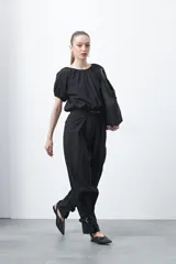 Pantalón baggy negro de silueta relajada con volumen amplio y caída fluida. Presenta detalles de ajuste con hebillas metálicas en el bajo y un cinturón de tela con hebilla metálica en la cintura.