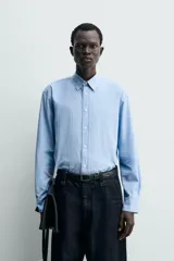 Camisa de algodón celeste con rayas verticales finas en blanco, de corte relajado (relaxed fit), cuello solapa y manga larga con puño abotonado.