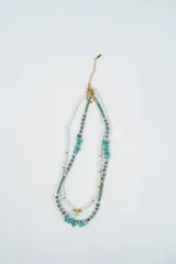 Set de dos collares, uno compuesto por perlas blancas pequeñas y otro por cuentas de piedra turquesa irregular, cuentas verdes y un dije de estrella plateada.