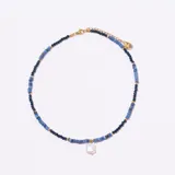Gargantilla corta estilo choker compuesta por cuentas facetadas en tonos de azul oscuro y azul claro, separadas por pequeñas cuentas doradas. Cuelga un dije de perla barroca blanca cuadrada. El cierre es de metal dorado con cadena de ajuste y dije con logo grabado.