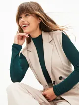 Chaleco beige con solapas, doble botonadura, lazo para atar en la cintura y bolsillos delanteros.