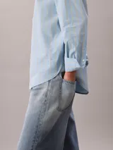 Camisa de corte clásico con estampado de rayas verticales en tonos celeste y amarillo. Presenta cuello en punta, mangas largas con hombros caídos y cierre frontal mediante botones.