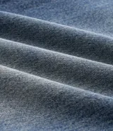 Pantalón de jean azul con lavado desgastado, de corte baggy holgado, tiro medio y diseño con recortes curvos en las piernas. Cuenta con presillas para cinturón, bolsillos clásicos y cierre frontal con botón y cremallera.