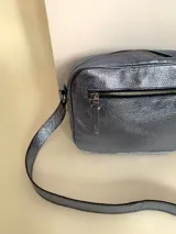 Bandolera rectangular de cuero azul metalizado con correa larga regulable. Cuenta con un bolsillo frontal con fuelle y un bolsillo trasero con cierre.