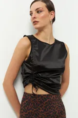 Musculosa negra de satén con cuello redondo y cordón ajustable en el lateral izquierdo para fruncir la prenda.