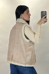 Chaleco tipo gamulán color marrón con interior y bordes de corderito sintético color crema. Presenta cierre frontal y bolsillos laterales con cremalleras metálicas, además de detalles de tiras de cuero sintético.