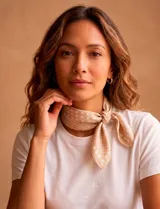 Pañuelo cuadrado de satén en color beige con estampado de lunares blancos de distintos tamaños. Presenta un diseño suave y ligero, ideal para anudar al cuello.